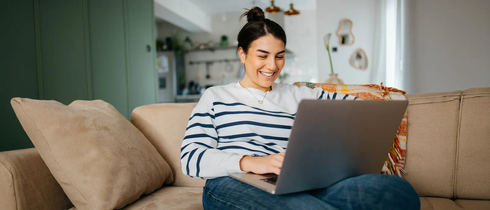 Woman in white and blue stripe shirt using laptop as she sits on the sofa.